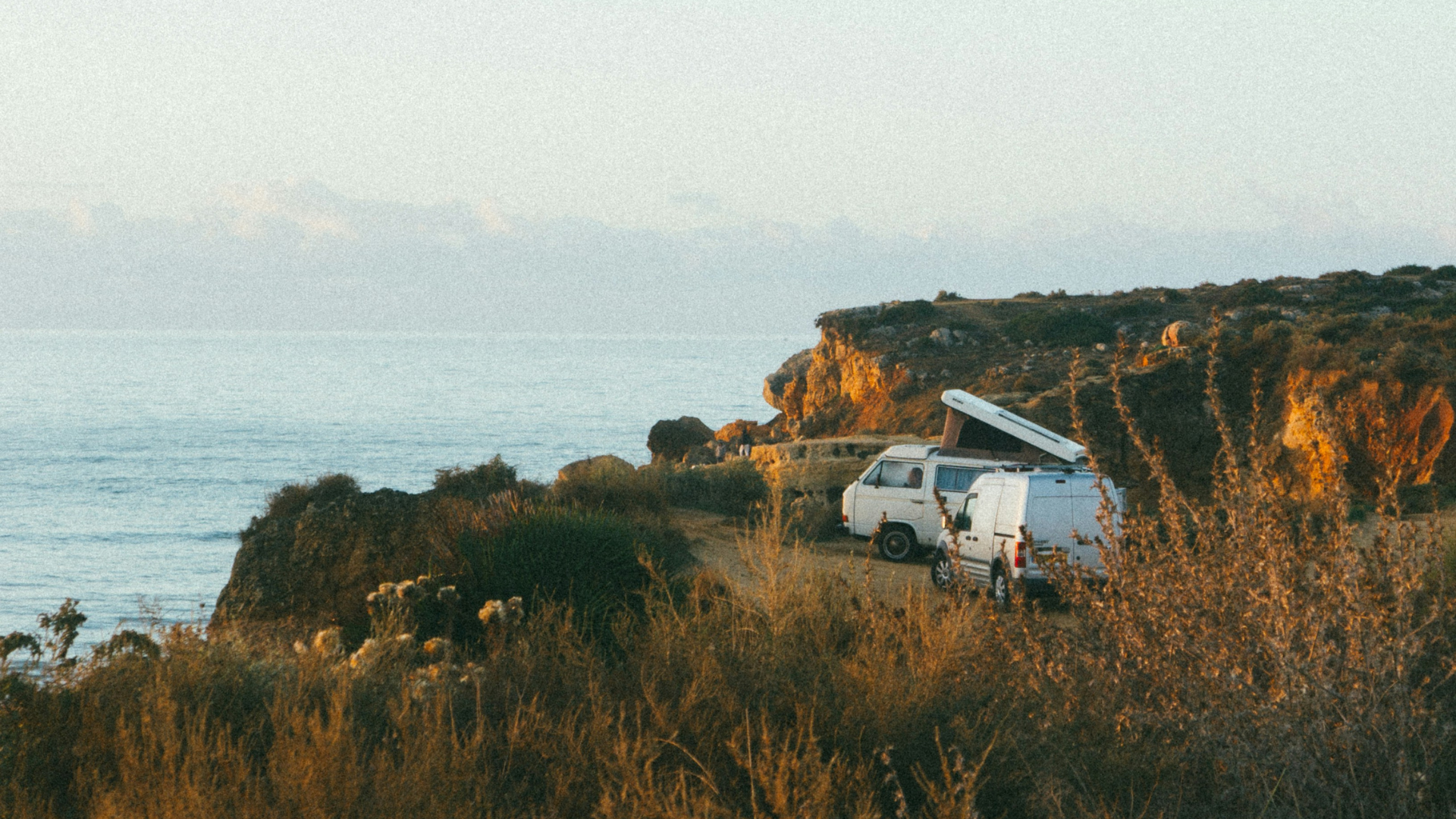 Aerial view of three campervans parked on a cliff above the ocean